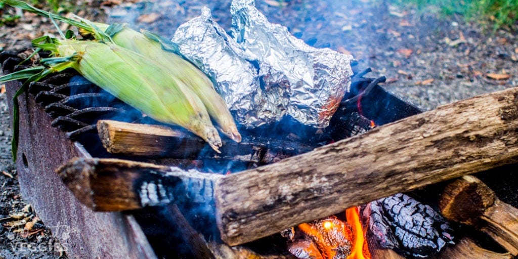 Campfire foil packets cooking with fresh sweet corn over indirect heat.