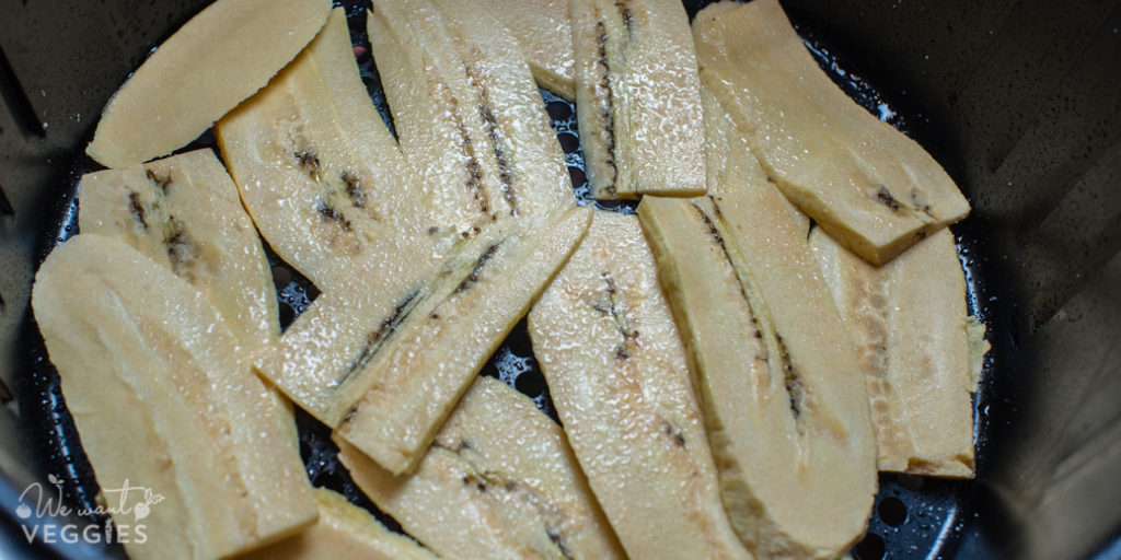 Plantain strips laying flat in the airfryer basket.