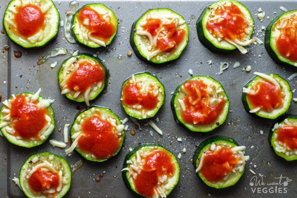 Zucchini rounds on baking pan with tomato sauce