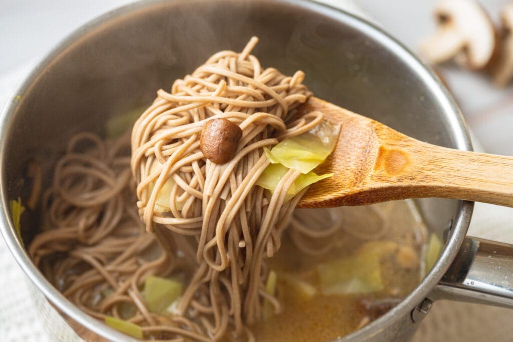 Soba noodles on spoon over pot.