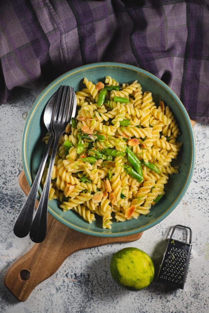 Fusilli with green beans and almonds in a bowl with spoon and fork.