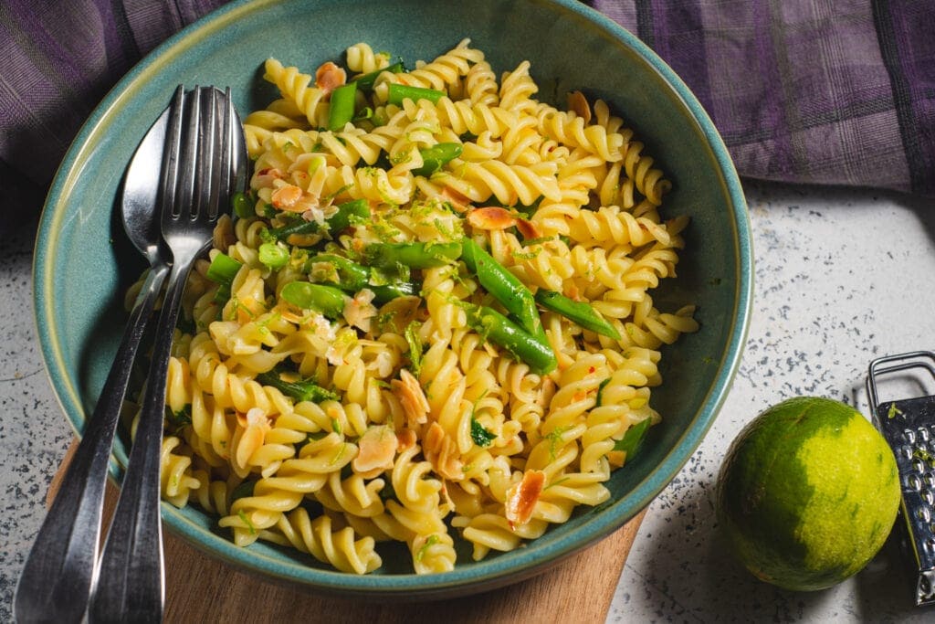 Fusilli with green beans and almonds in a bowl with spoon and fork.